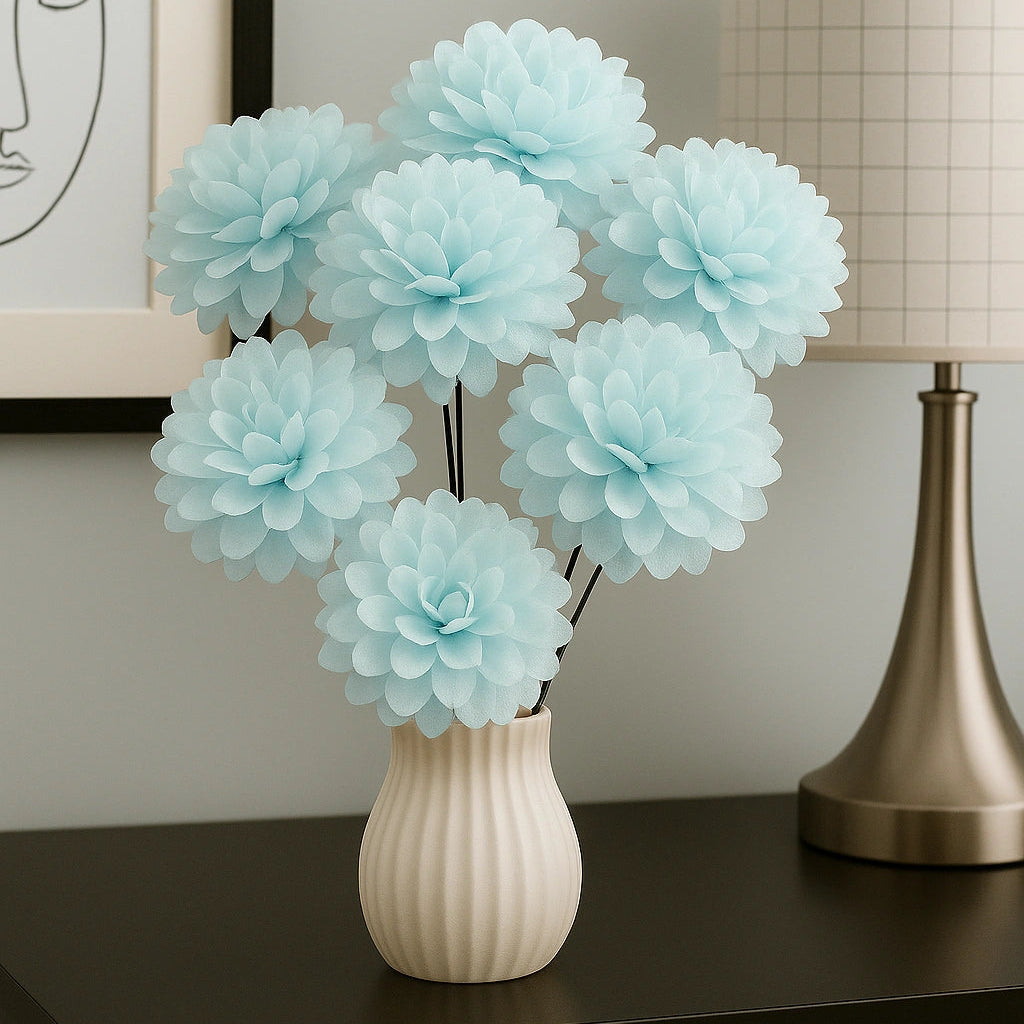 Light blue flowers in a white vase on a dark surface with a lamp and framed picture in the background.