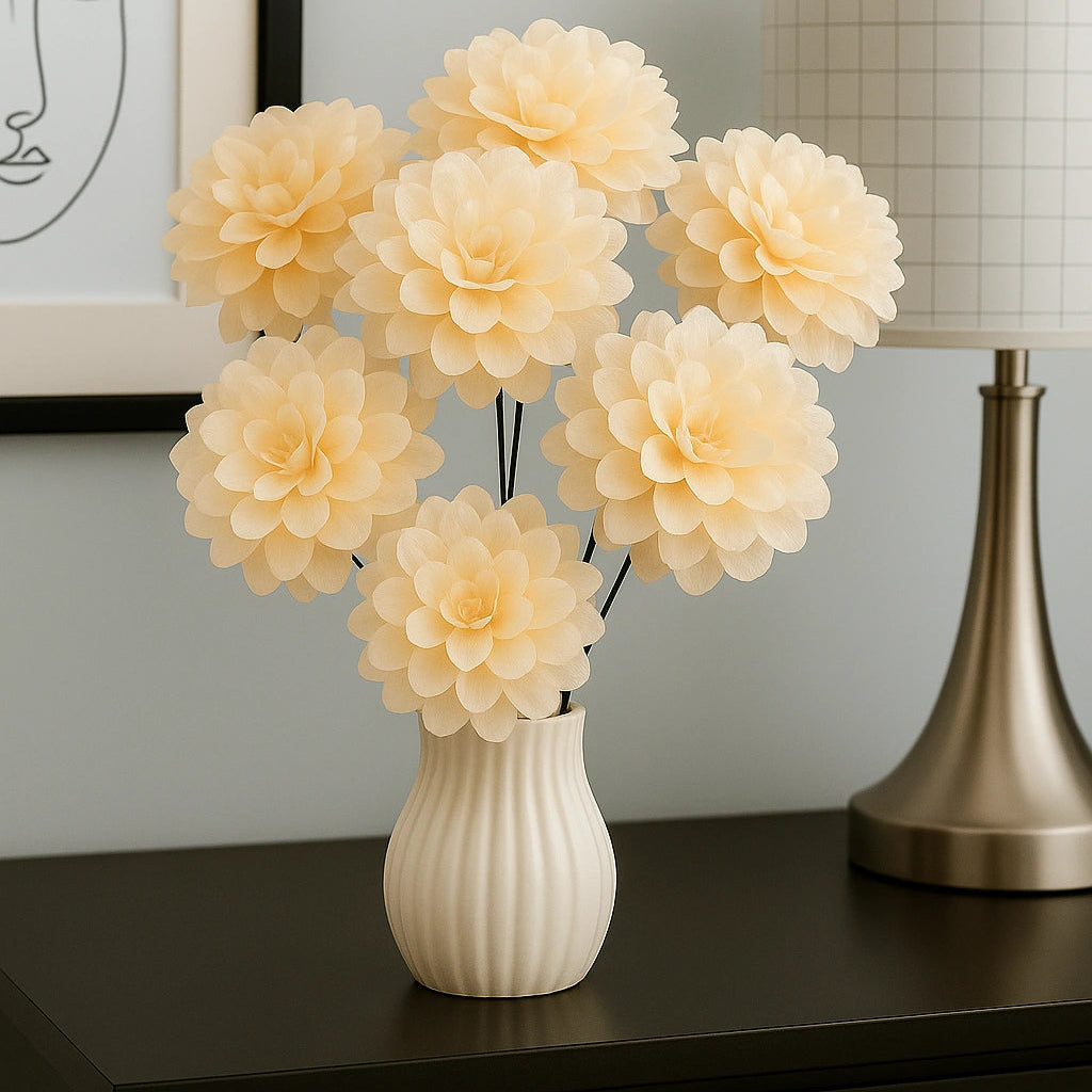 Cream-colored flowers in a white vase on a dark surface with a lamp and framed picture in the background.