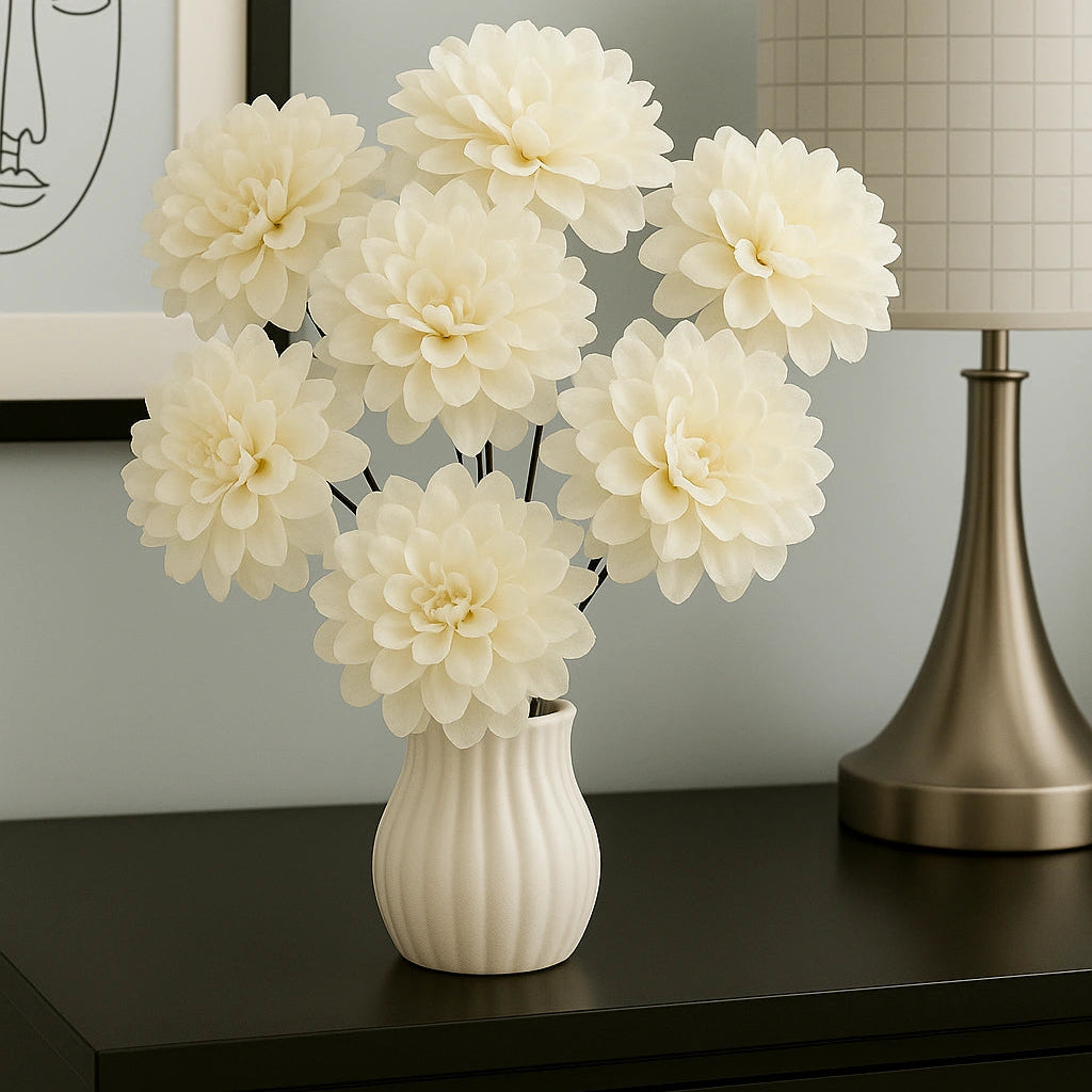 White flowers in a vase on a dark surface with a lamp and framed picture in the background.