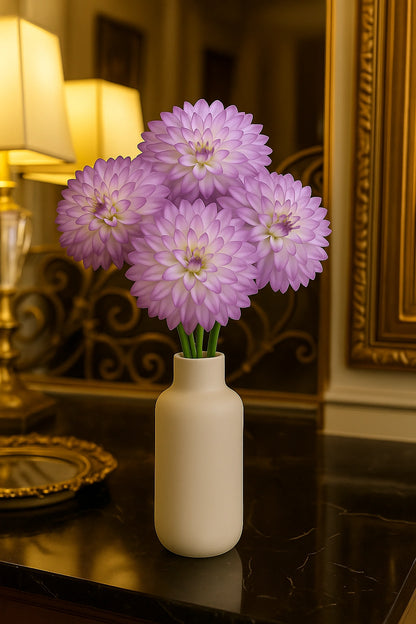 White vase with purple flowers on a reflective surface with a decorative background