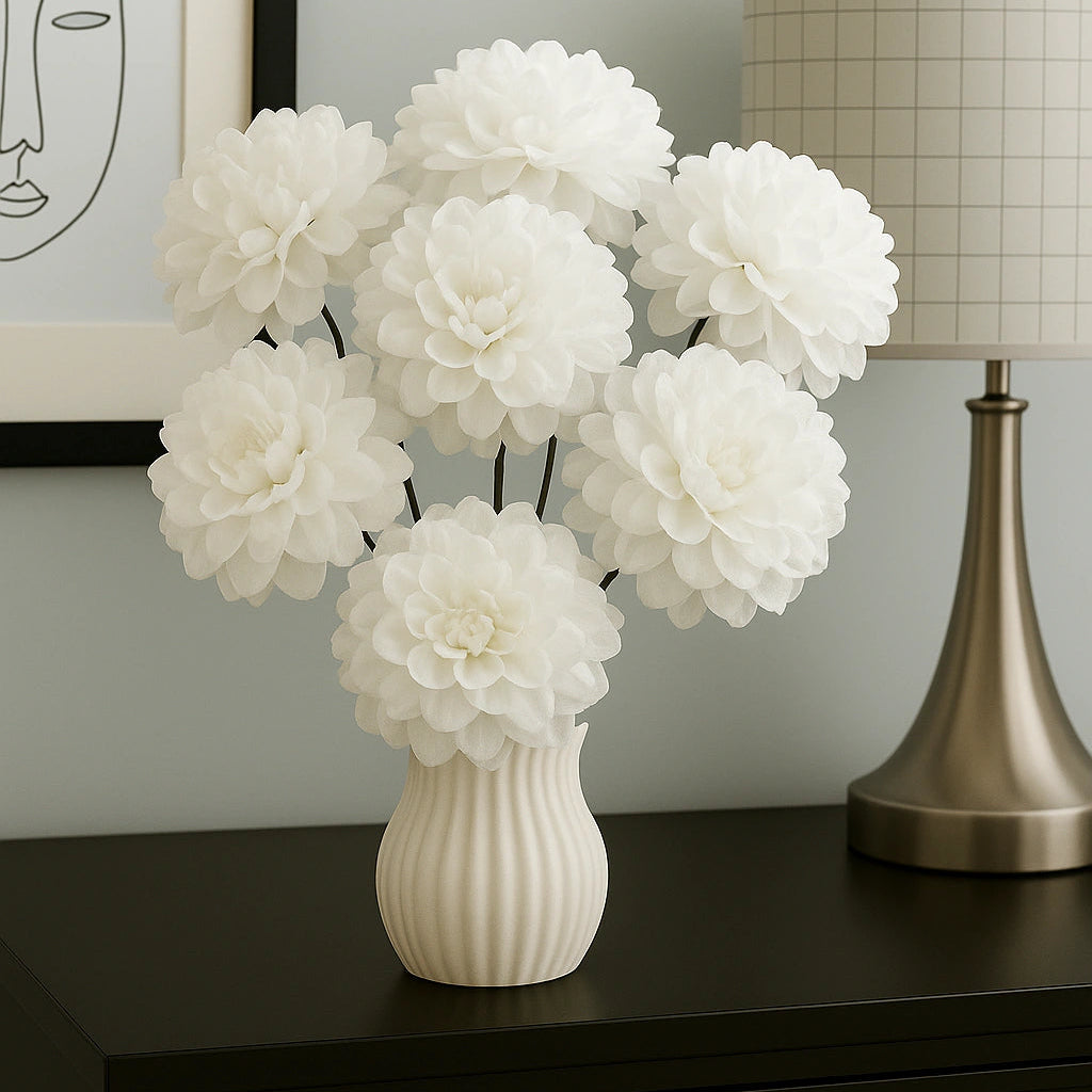White flowers in a vase on a dark surface with a lamp and framed picture in the background.