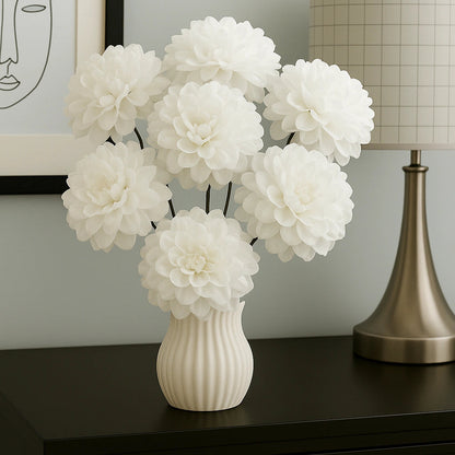 White flowers in a vase on a dark surface with a lamp and framed picture in the background.