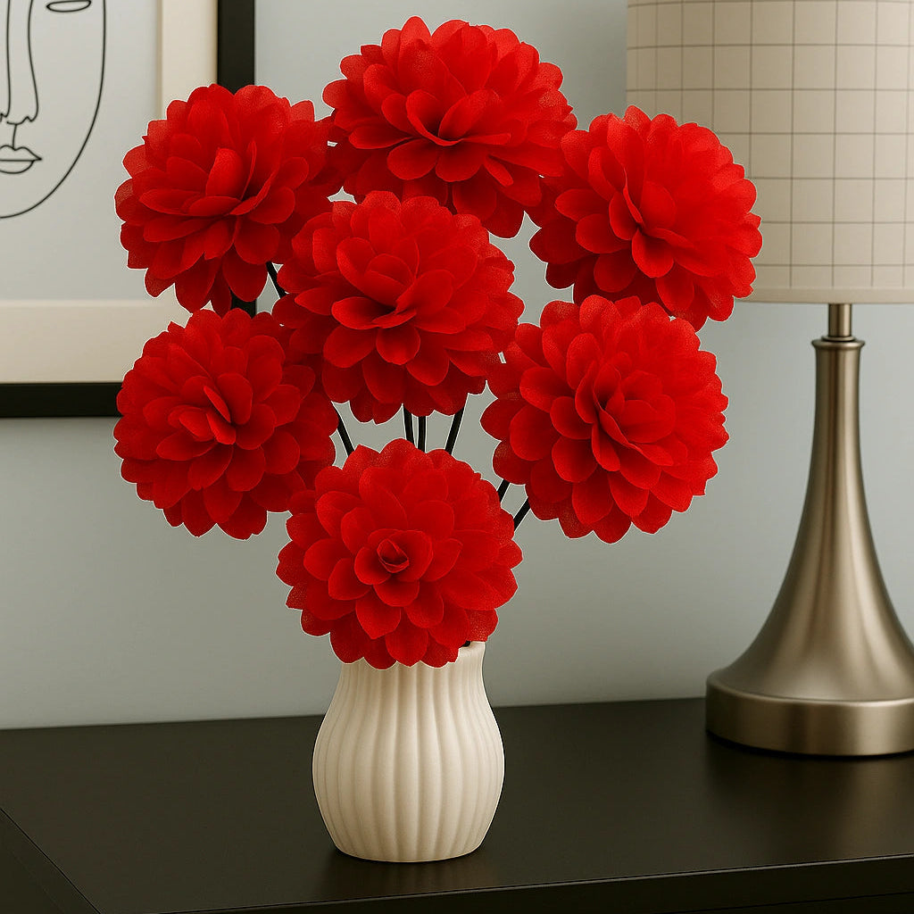 Red flowers in a white vase on a dark surface with a lamp and framed picture in the background.