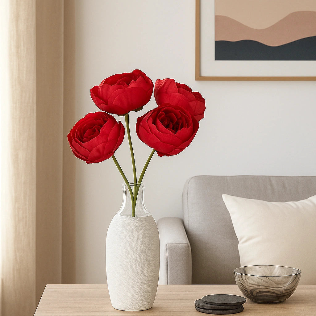 Red flowers in a white vase on a wooden side table with a sofa and wall art in the background.