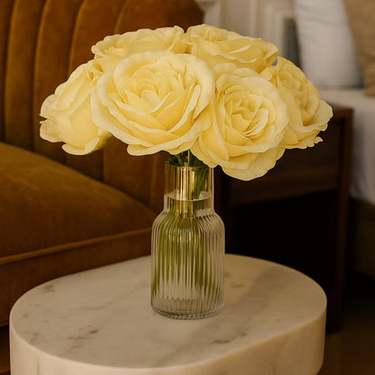 Bouquet of yellow roses in a clear vase on a marble table with a blurred background