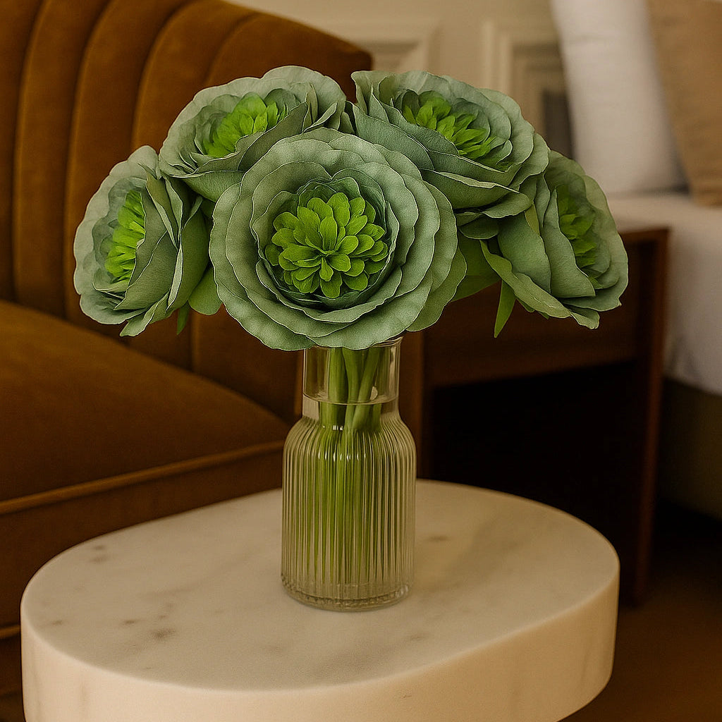 Green floral arrangement in a vase on a marble table with a blurred indoor setting.